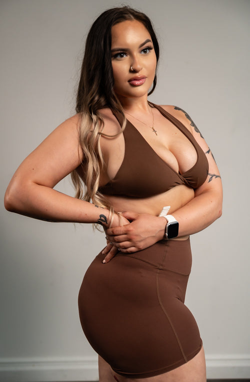Woman wearing a brown sports bra and shorts against a plain background